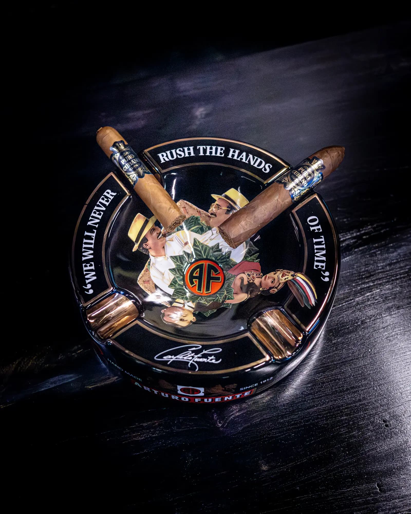 Two cigars resting in an Arturo Fuente ashtray on dark wood
